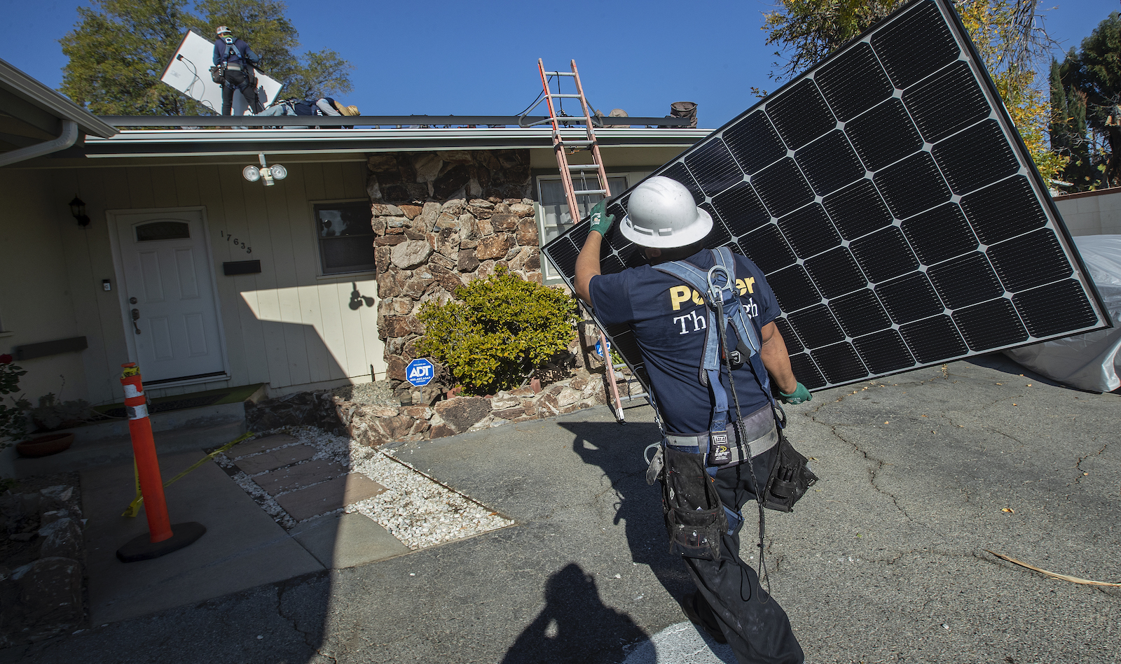 solar panel installer carries a solar panel toward a house