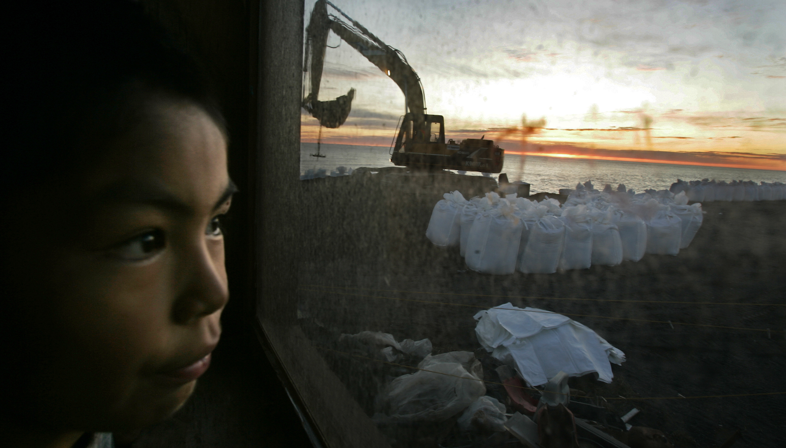 A boy watches workers fill sandbags for a seawall to shield his island from the Chukchi Sea.