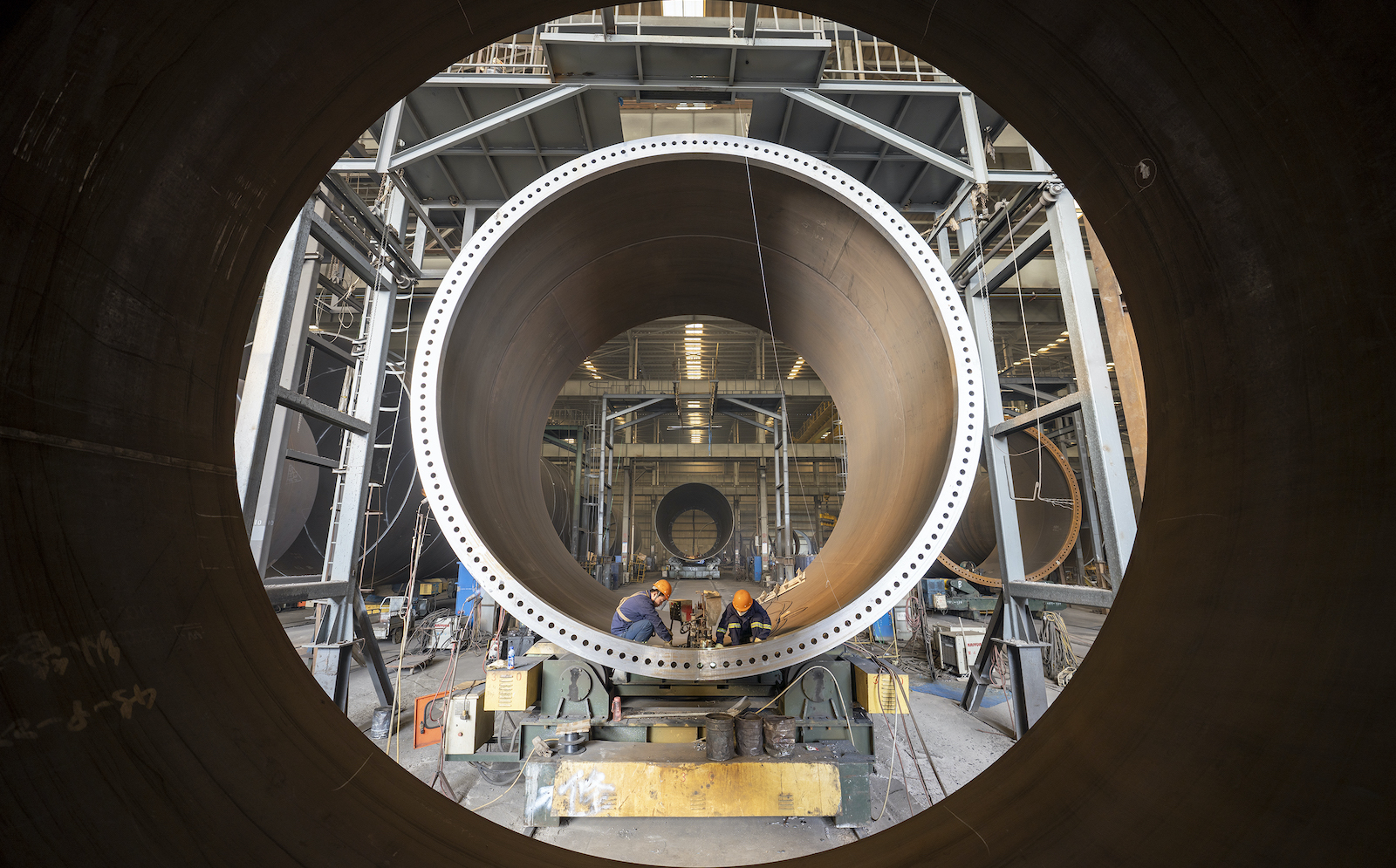 The mouth of a hollow wind turbine monopile with workers welding inside