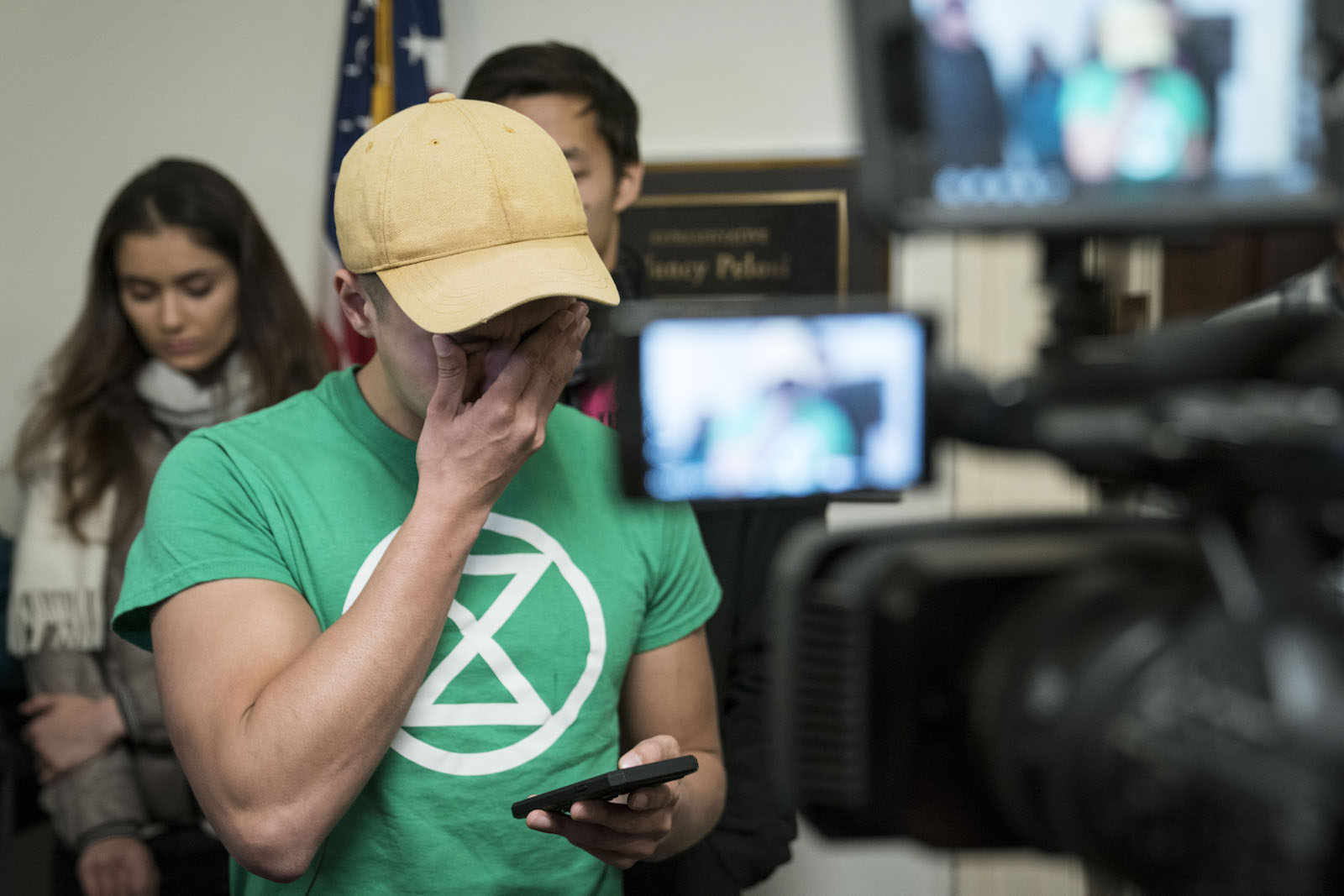 a man in a green shirt with an extinction rebellion logo on it holds a hand over his teary eyes while appearing to read off his phone