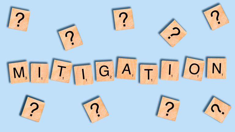 The word mitigation spelled out with Scrabble tiles surrounded by question marks
