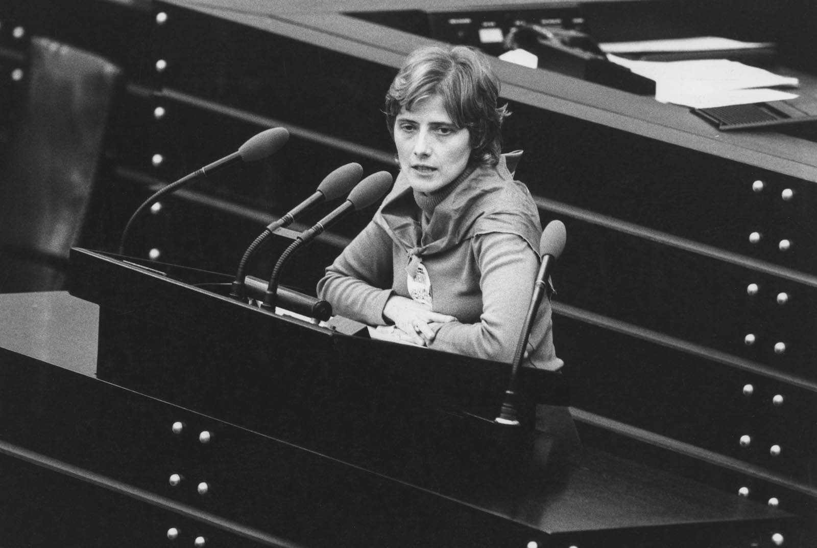 a black and white photo of a woman with short hair sitting in front of a microphone talking
