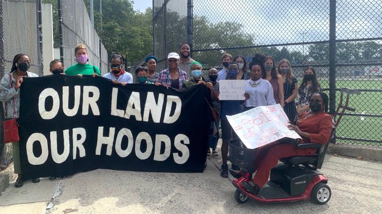 Community organizers with a sign reading, "Our land, our hoods."
