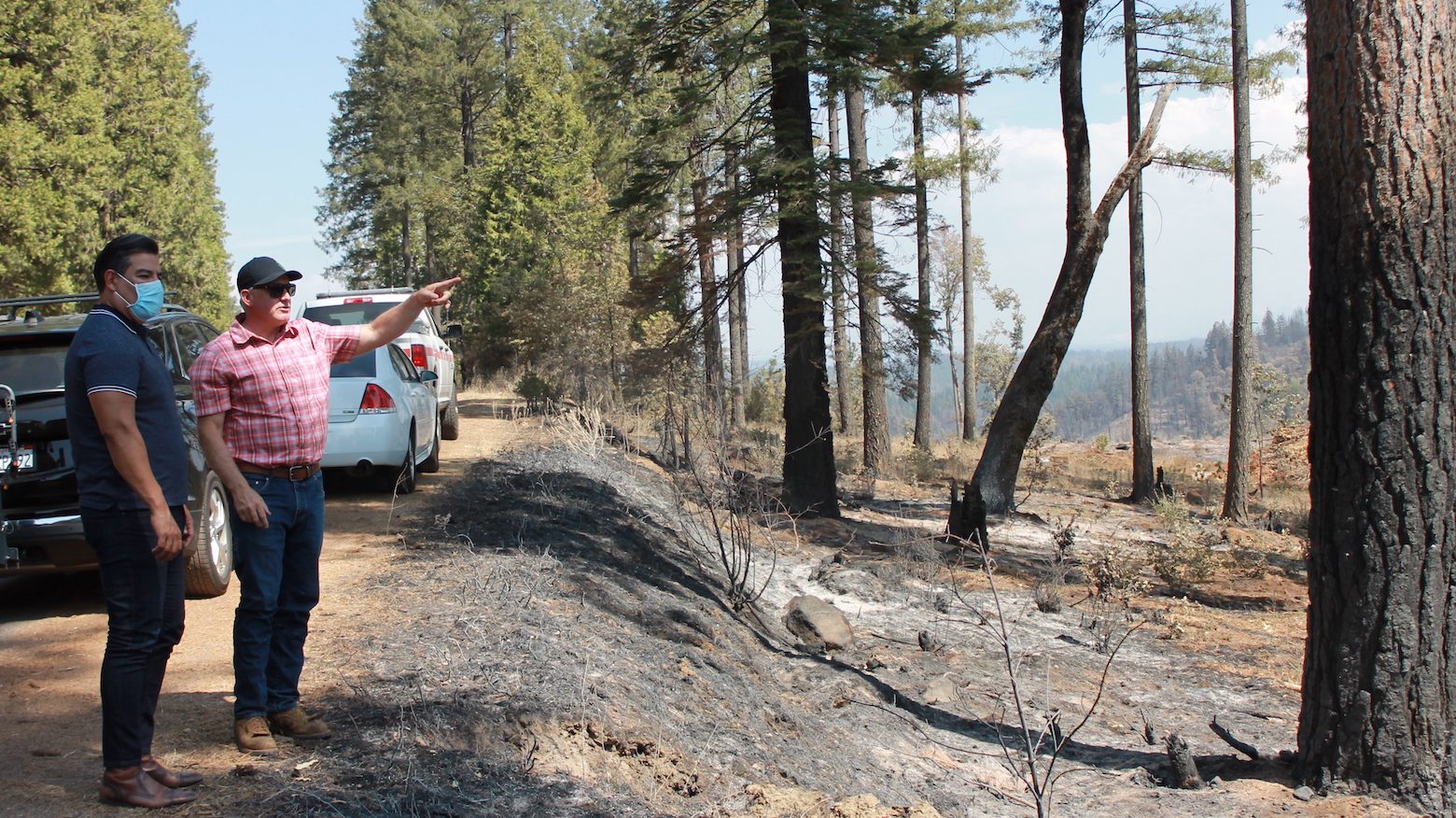 Ricardo Lara and Mark Egbert look over a shaded fuel break where firefighters were able to stop the Caldor Fire.
