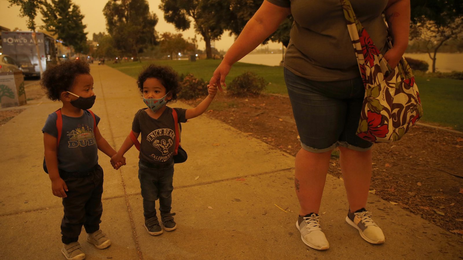Emory and Henry Peters, 2, walk with their nanny Cynthia Chavez at Lake Merritt in Oakland, Calif., on Wednesday, Sept. 9, 2020. The unusual orange and red-hued skies were a result of smoke from the Northern California wildfires.