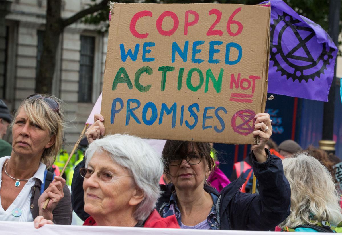 An activist holding a sign that reads "COP26 we need action not promises"