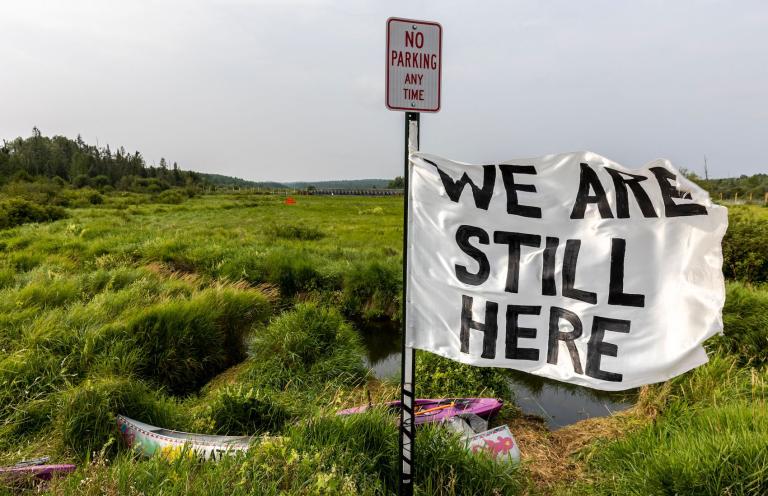 A sign reads "We are still here."