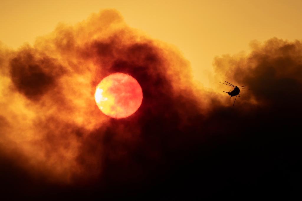 A firefighting helicopter flies as smoke from the Alisal Fire shrouds the sun on October 13, 2021 near Goleta, California. Pushed by high winds, the Alisal Fire grew to 6,000 acres overnight, shutting down the much-traveled 101 Freeway along the Pacific Coast.