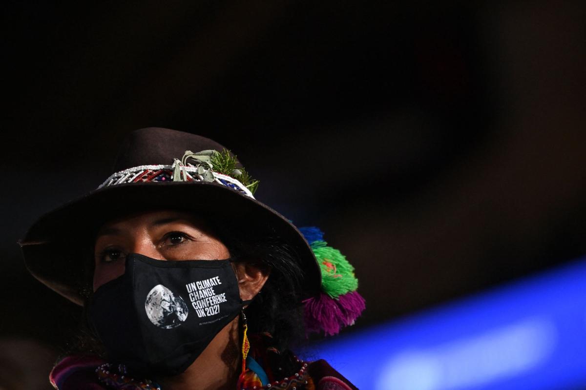A close up photograph of a woman wearing a traditional quichua hat and a mask with the words "UN CLIMATE CHANGE CONFERENCE UK 2021" printed on one side
