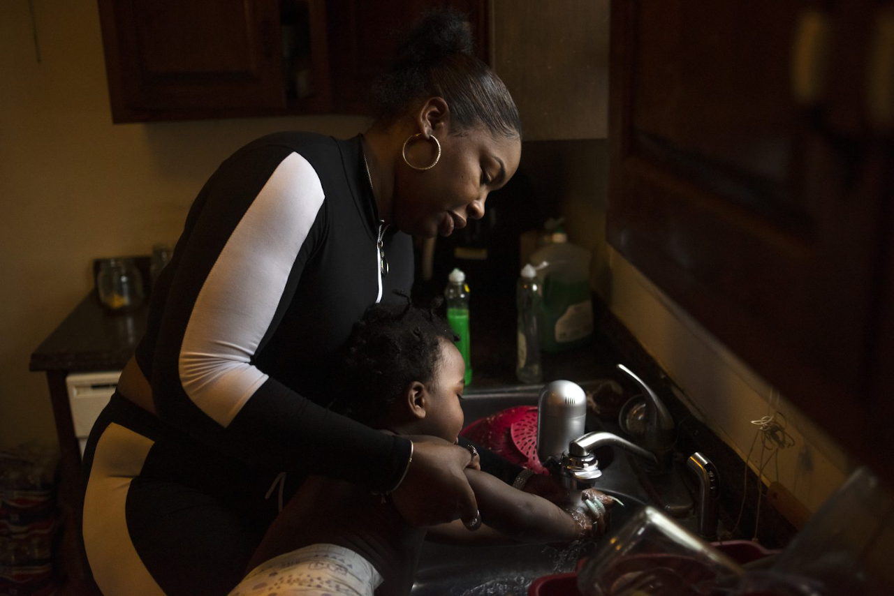 A Black mother and her child stand together at the kitchen sink in Flint, Michigan