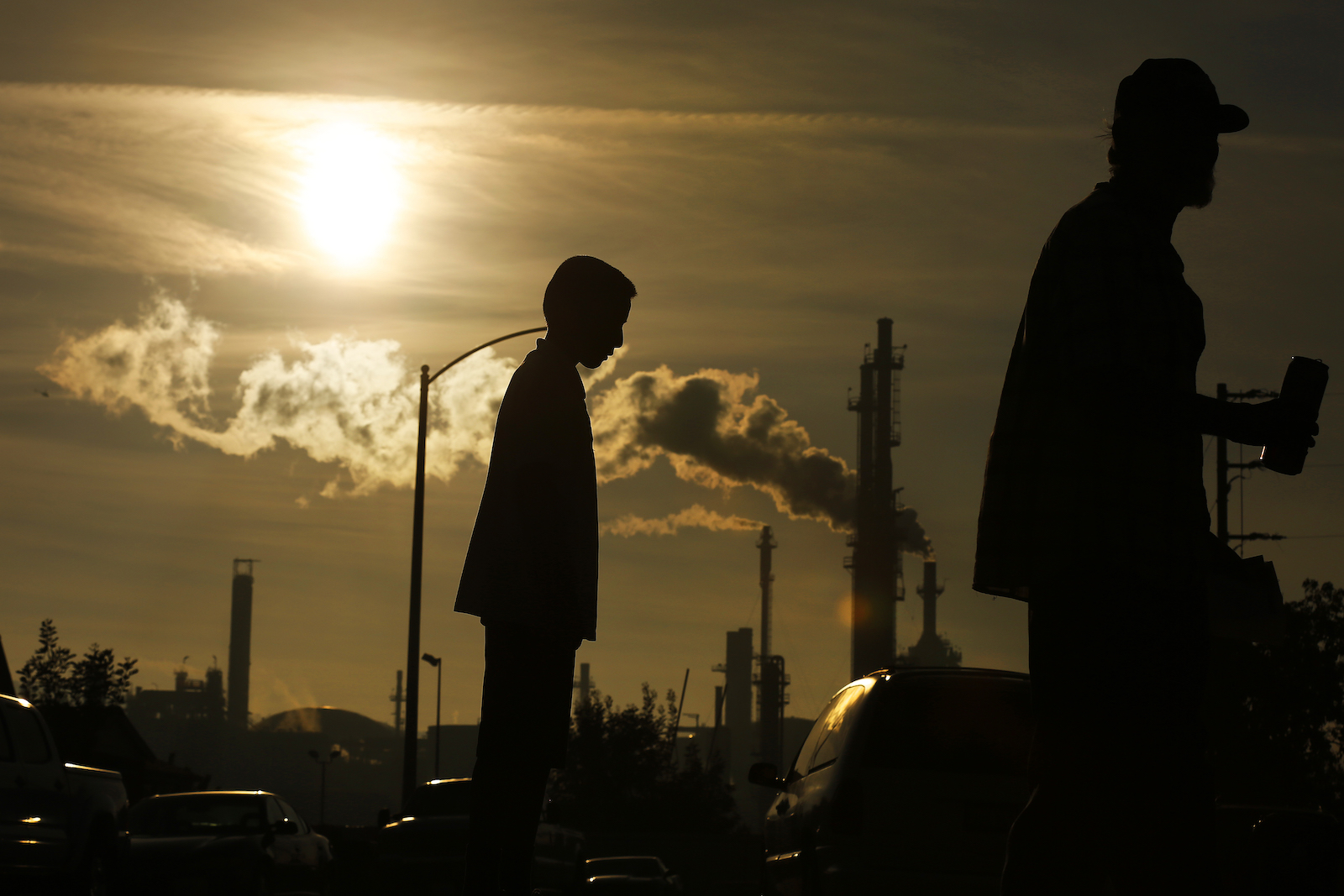 A silhouette of a young boy backdrops a plume of smoke rising from a refinery.