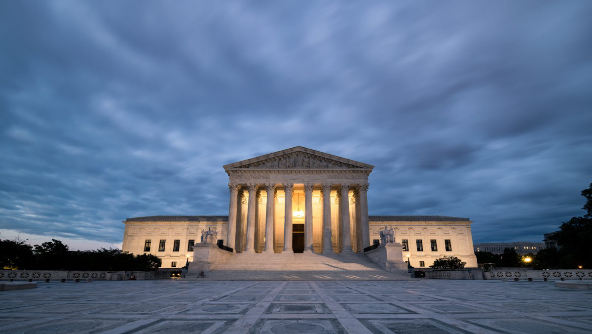 The lit-up front of the US Supreme Court beneath a cloudy, overcast sky
