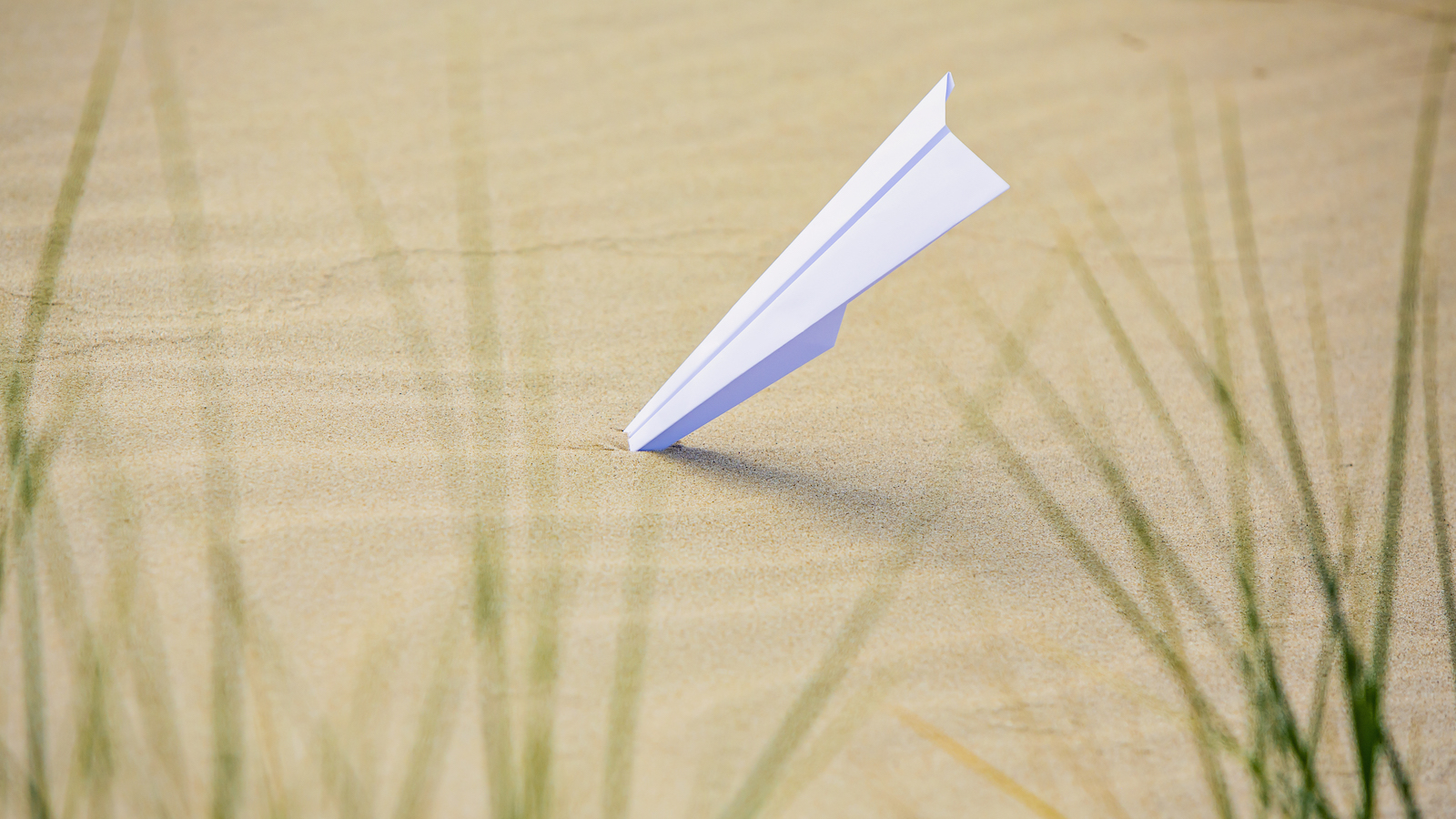 a paper airplane with its nose in the sand