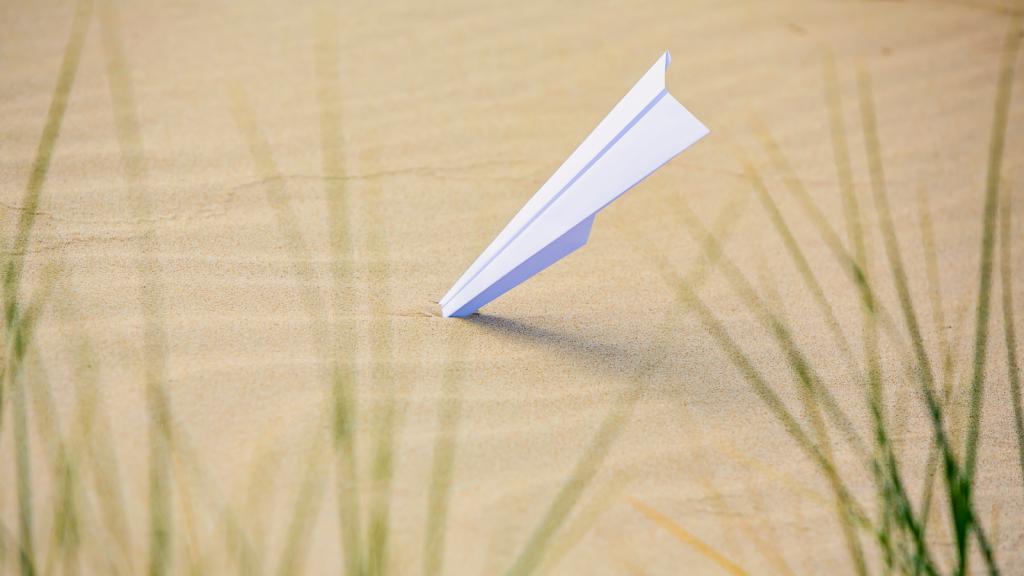 a paper airplane with its nose in the sand