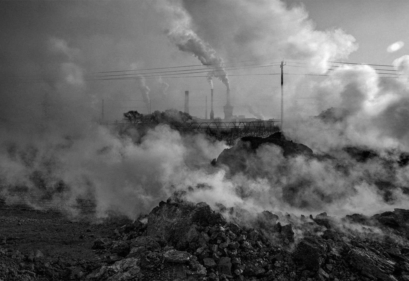 Smoke and steam rising from piles of coal waste with smokestacks in the background