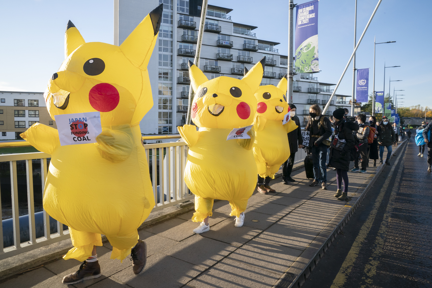 Protesters in inflatable pikachu costumes march holding signs that say "Japan, stop funding coal"
