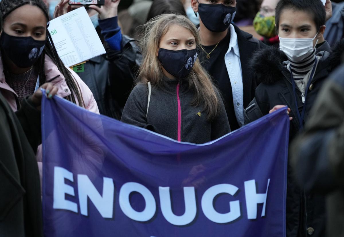 Climate activist Greta Thunberg at COP 26 holding a flag that reads "enough"