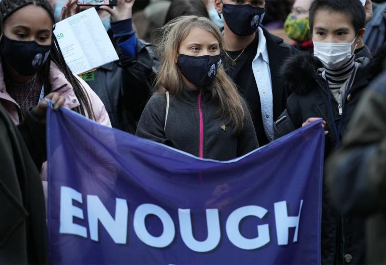Climate activist Greta Thunberg at COP 26 holding a flag that reads "enough"