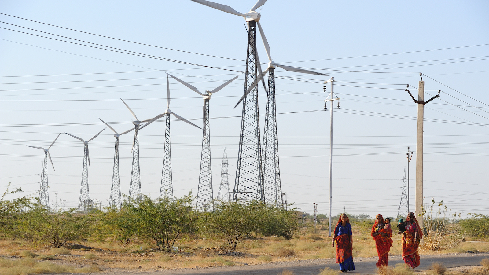 three women walk near a wind farm in India