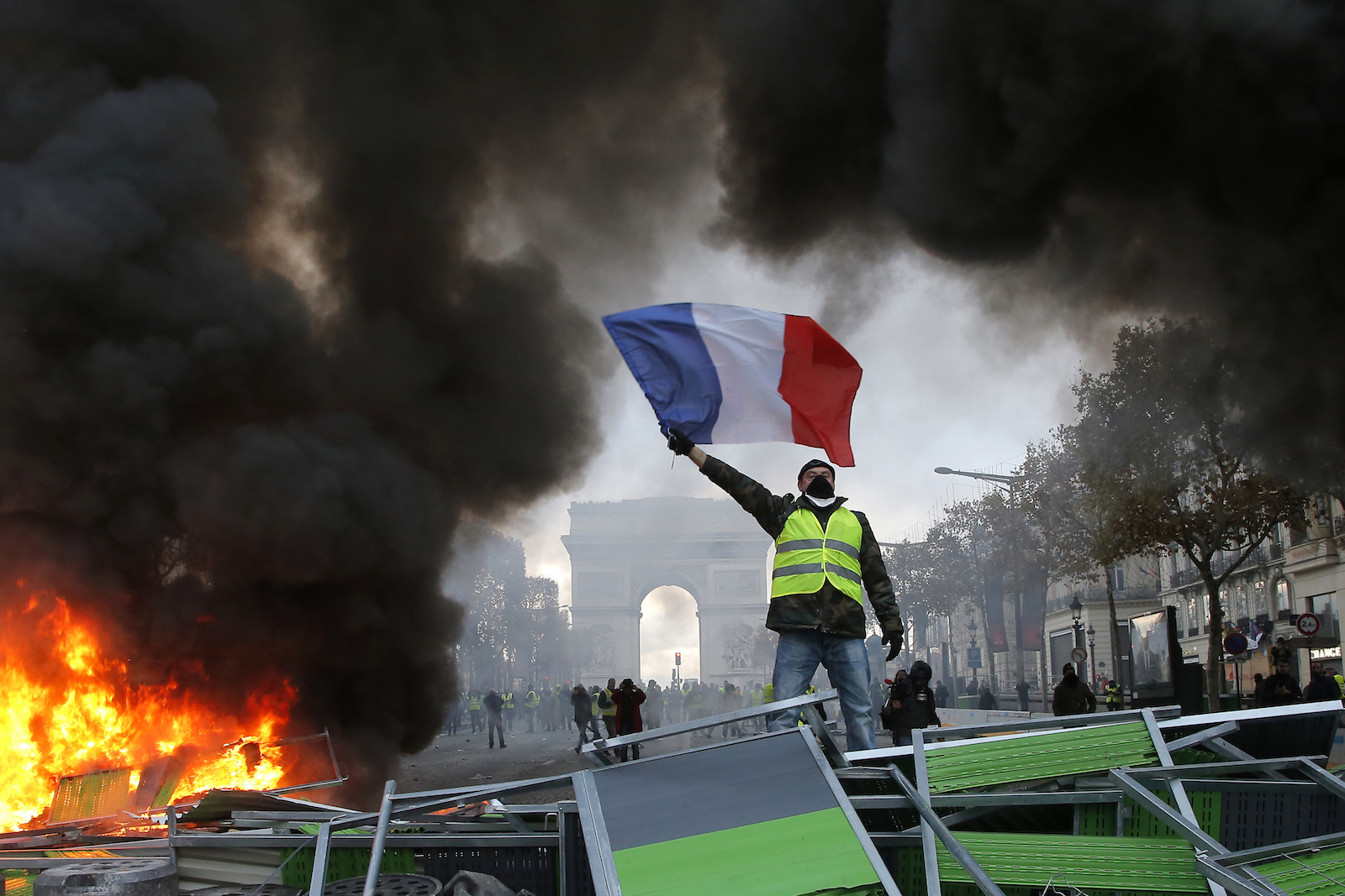 a man in a yellow vest waves a french flag in front of bright green barricades