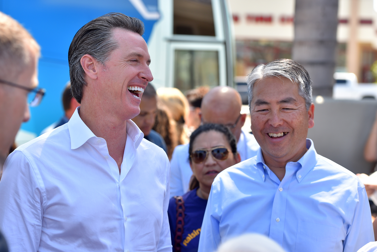 two men in button-up shirts smile in the middle of a sunny crowd