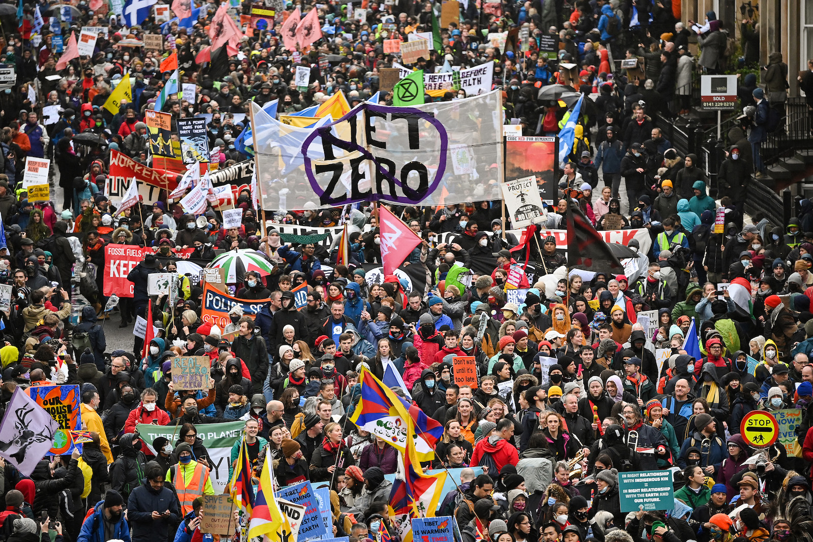 a large crowd of marchers with some holding a large sign with net zero inside a slashed circle
