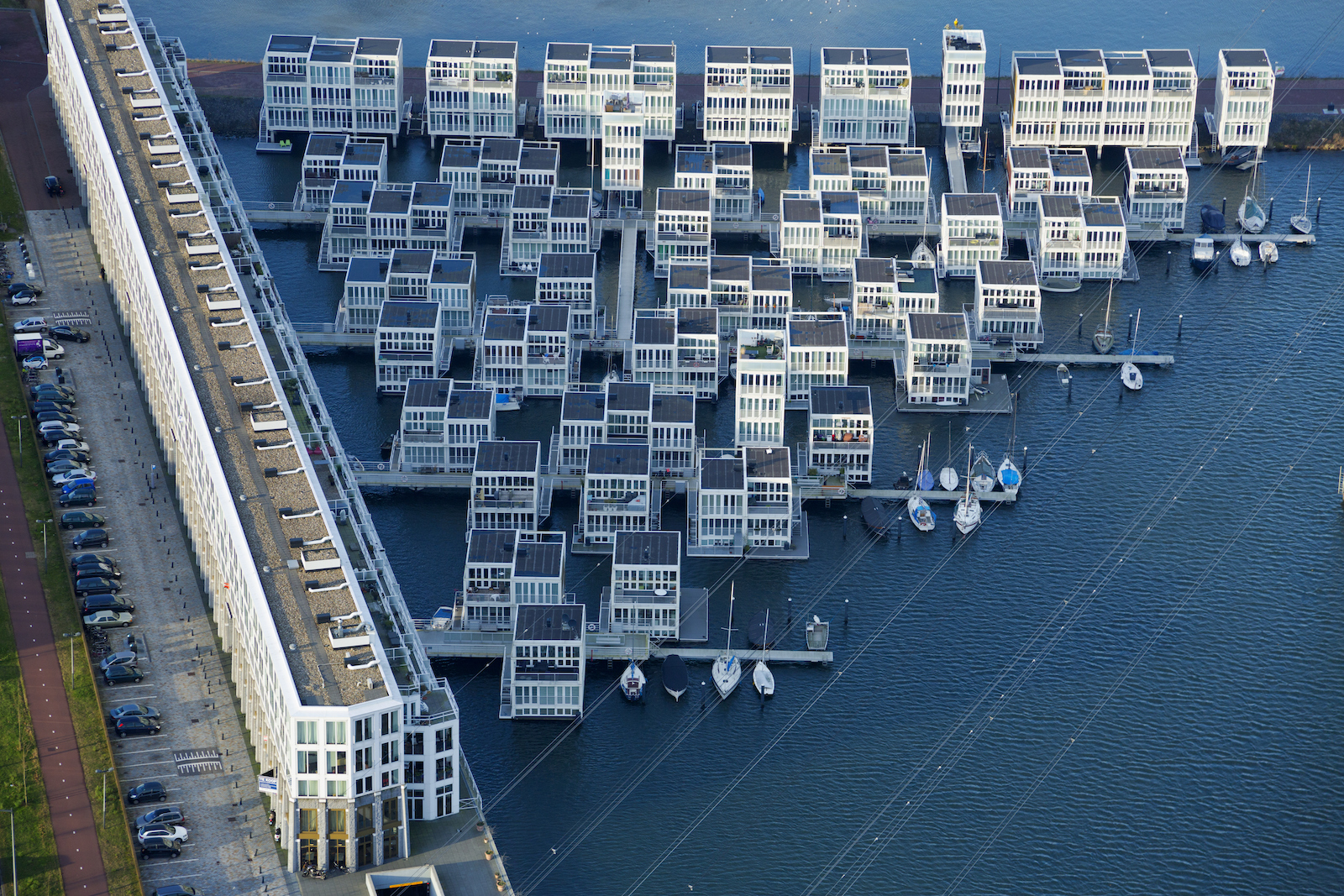 A floating community in the Netherlands lies on the coast in the IJburg section of Amsterdam. The houses are secured to large steel pilings with rolling collars that allow them to rise and fall with the water level, and sway slightly in strong winds. Each home has a small dock, communal walkways, and flexible utility connections. They are also required to be in balance, with heavy components, like kitchens and bathrooms positioned carefully on the lower floors for stability.