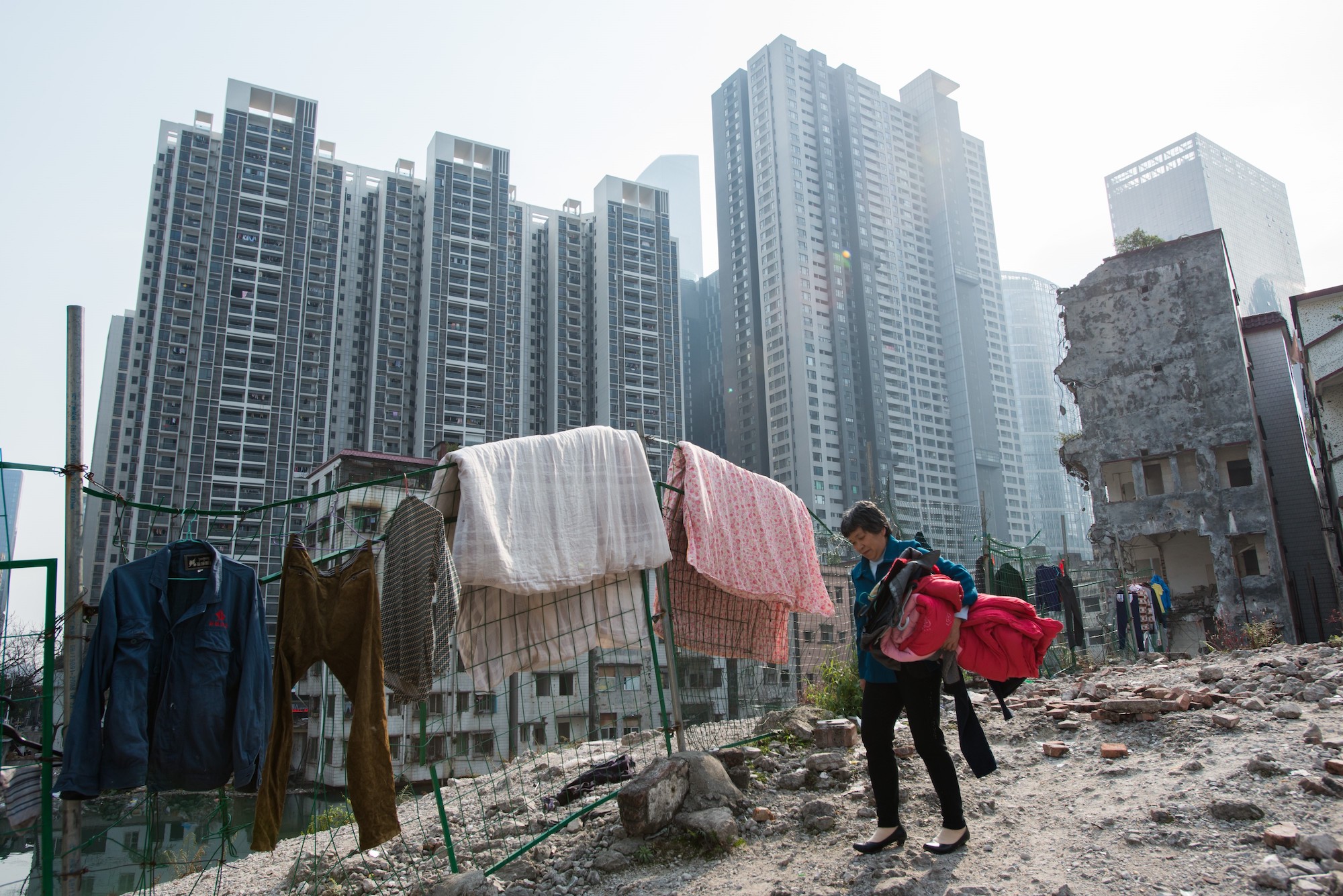 A woman does laundry near demolished residential buildings in Xiancun, a urban village in the Zhujiang New Town district of Guangzhou as high commercial and residential buildings rise in the distance.