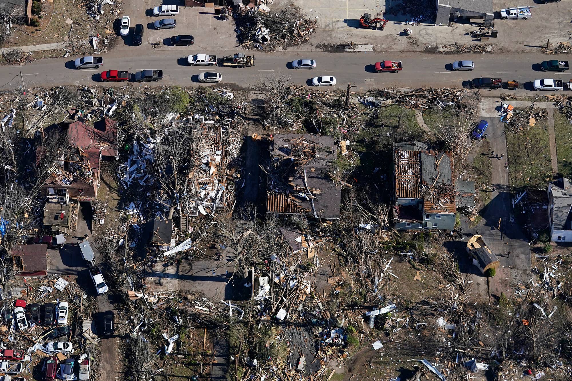 Cars drive past destroyed homes