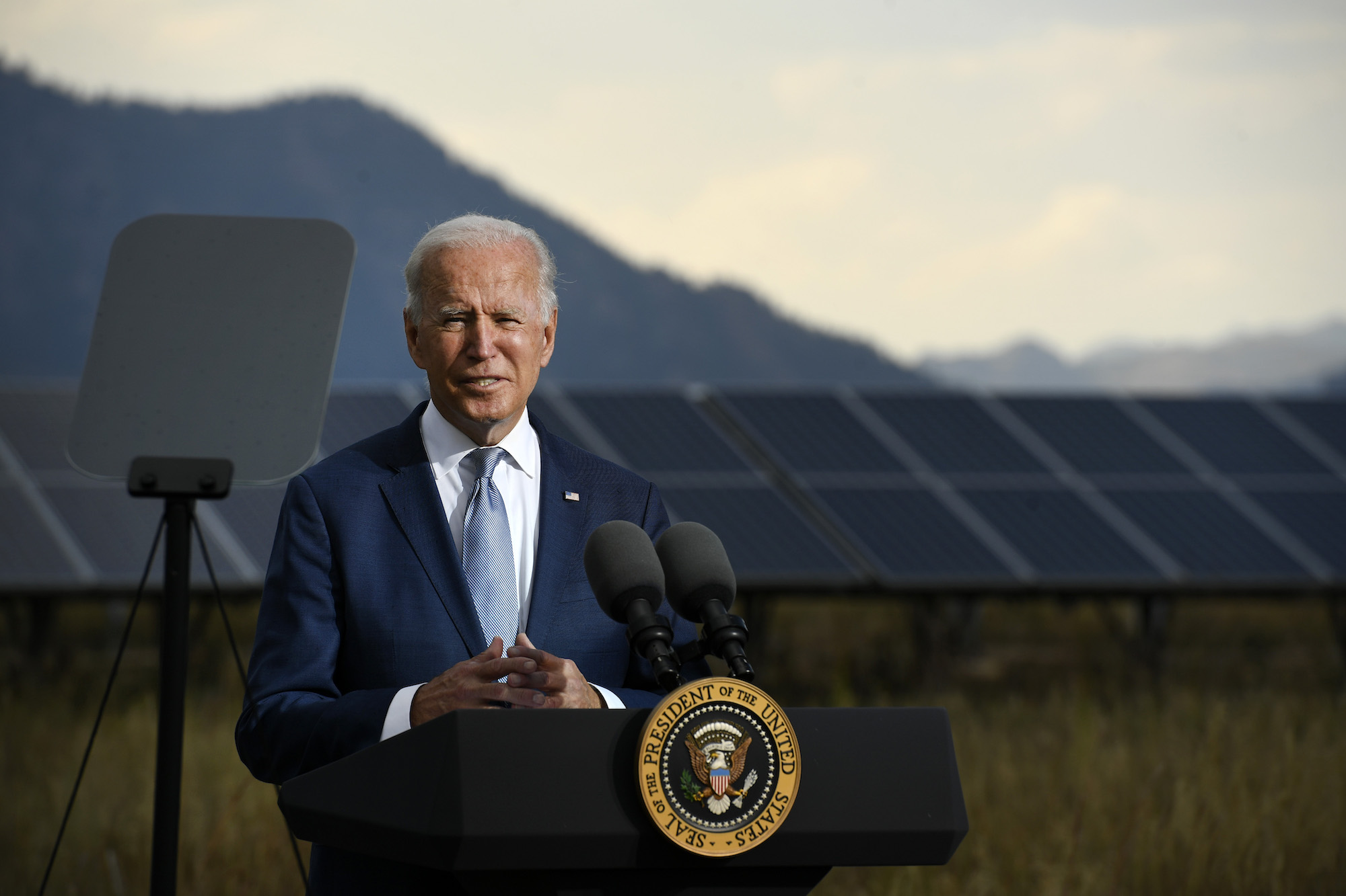 President Joe Biden stand on a podium in front of a large solar panel.