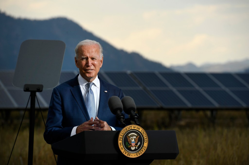 President Joe Biden stand on a podium in front of a large solar panel.