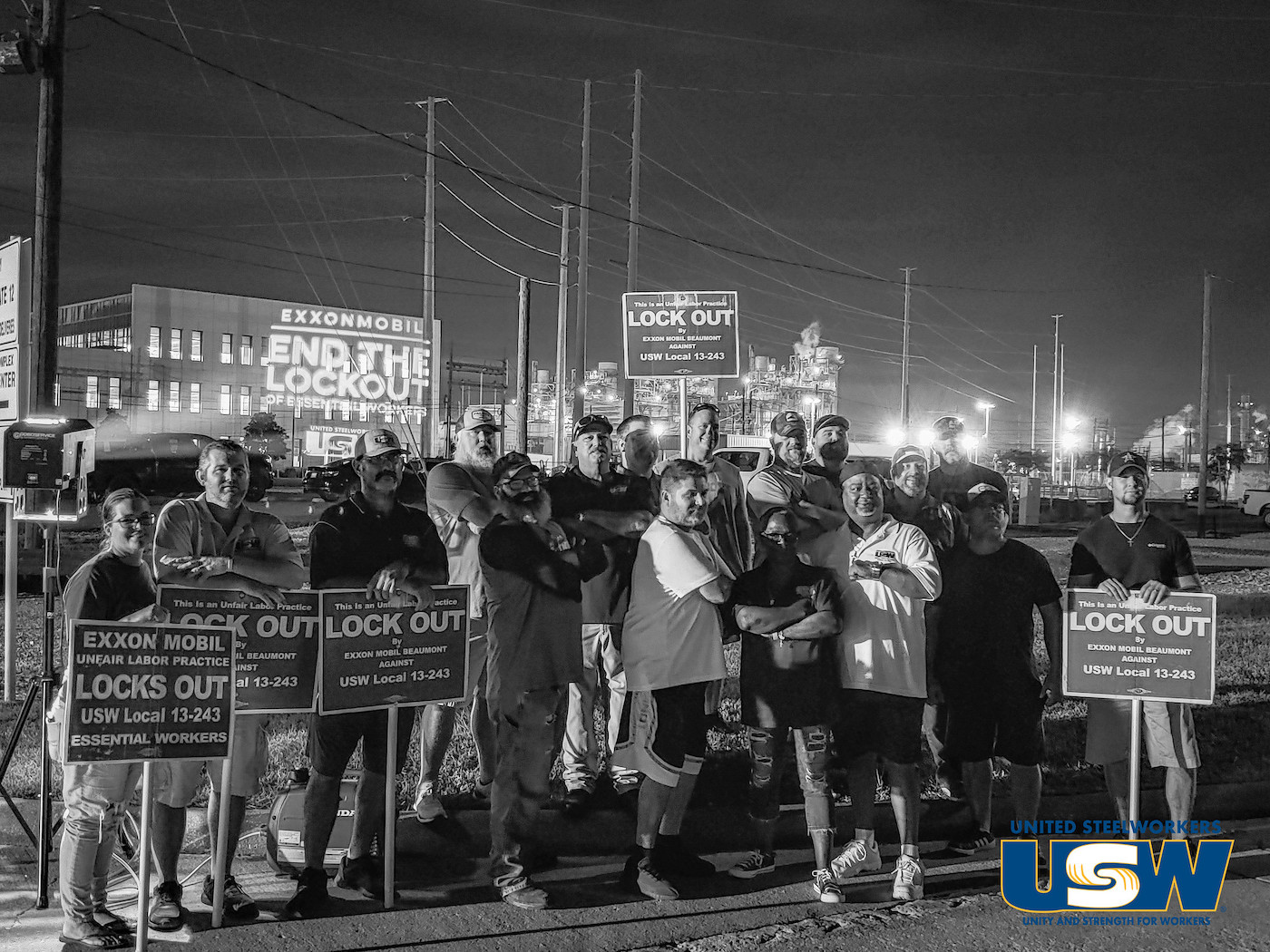 Workers stand in a group outside a refinery in Beaumont, Texas holding signs that say "end the lockout"
