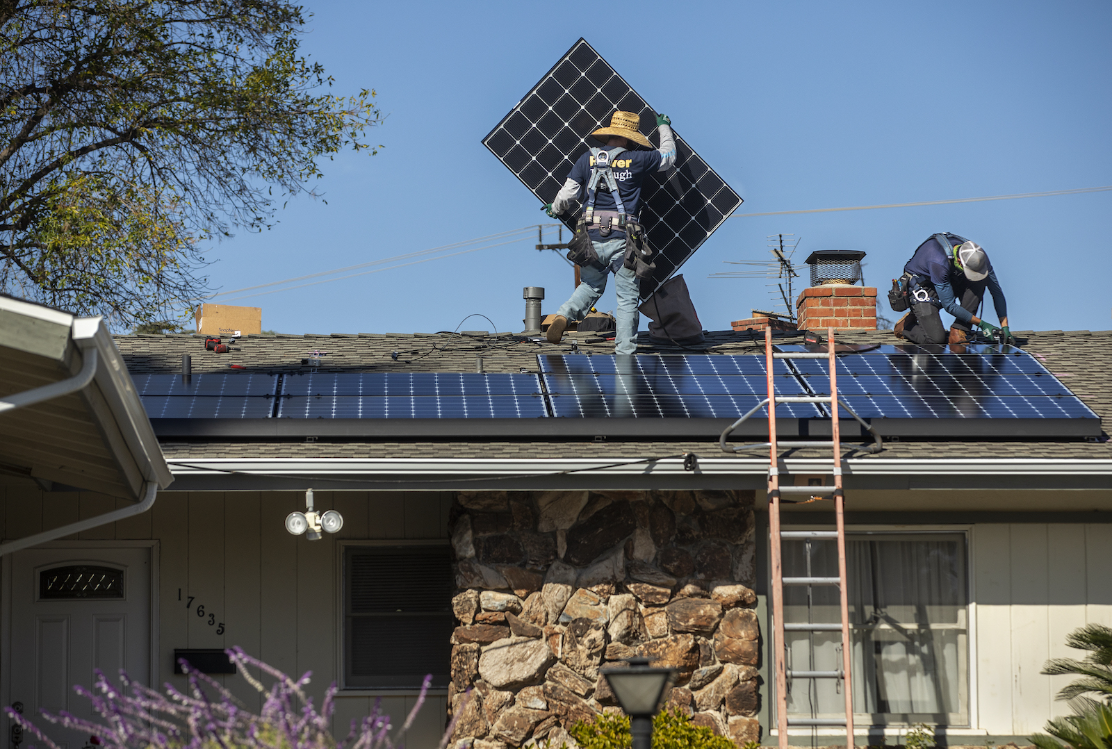 Two workmen install solar panels on a suburban house.