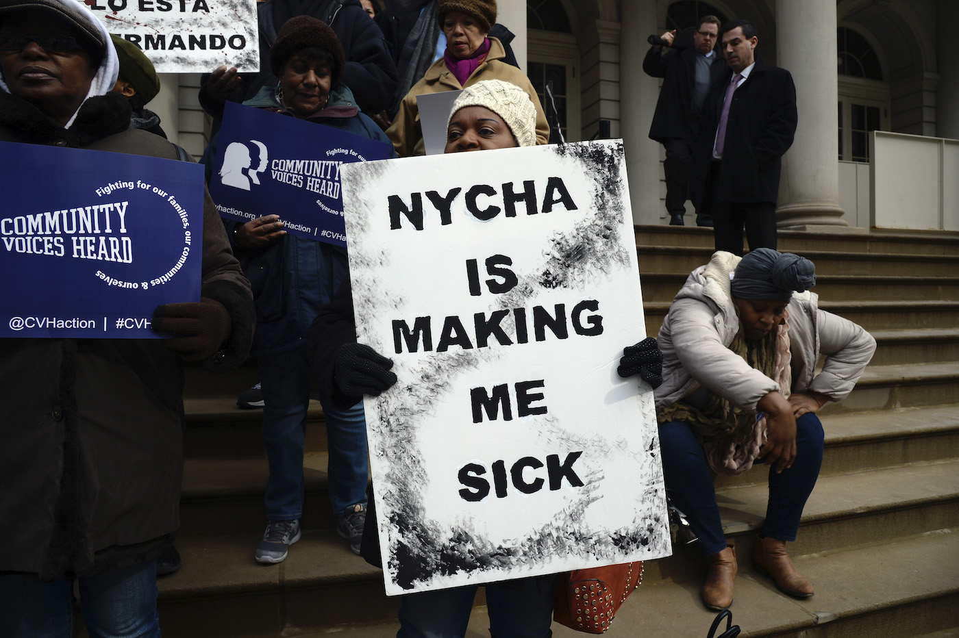Woman at rally holds sign that says NYCHA is making me sick
