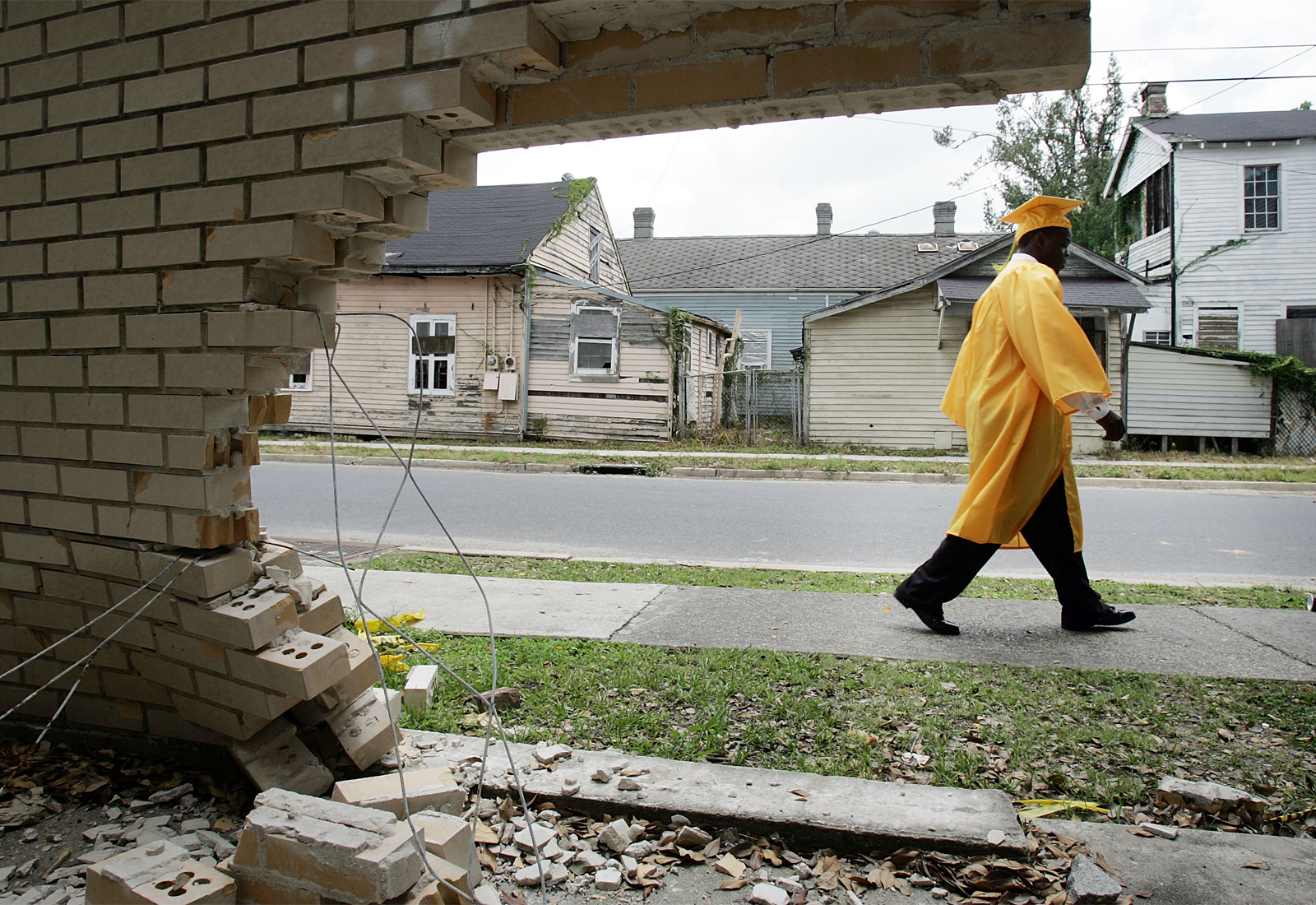 High school graduate walking past wall damaged by Hurricane Katrina