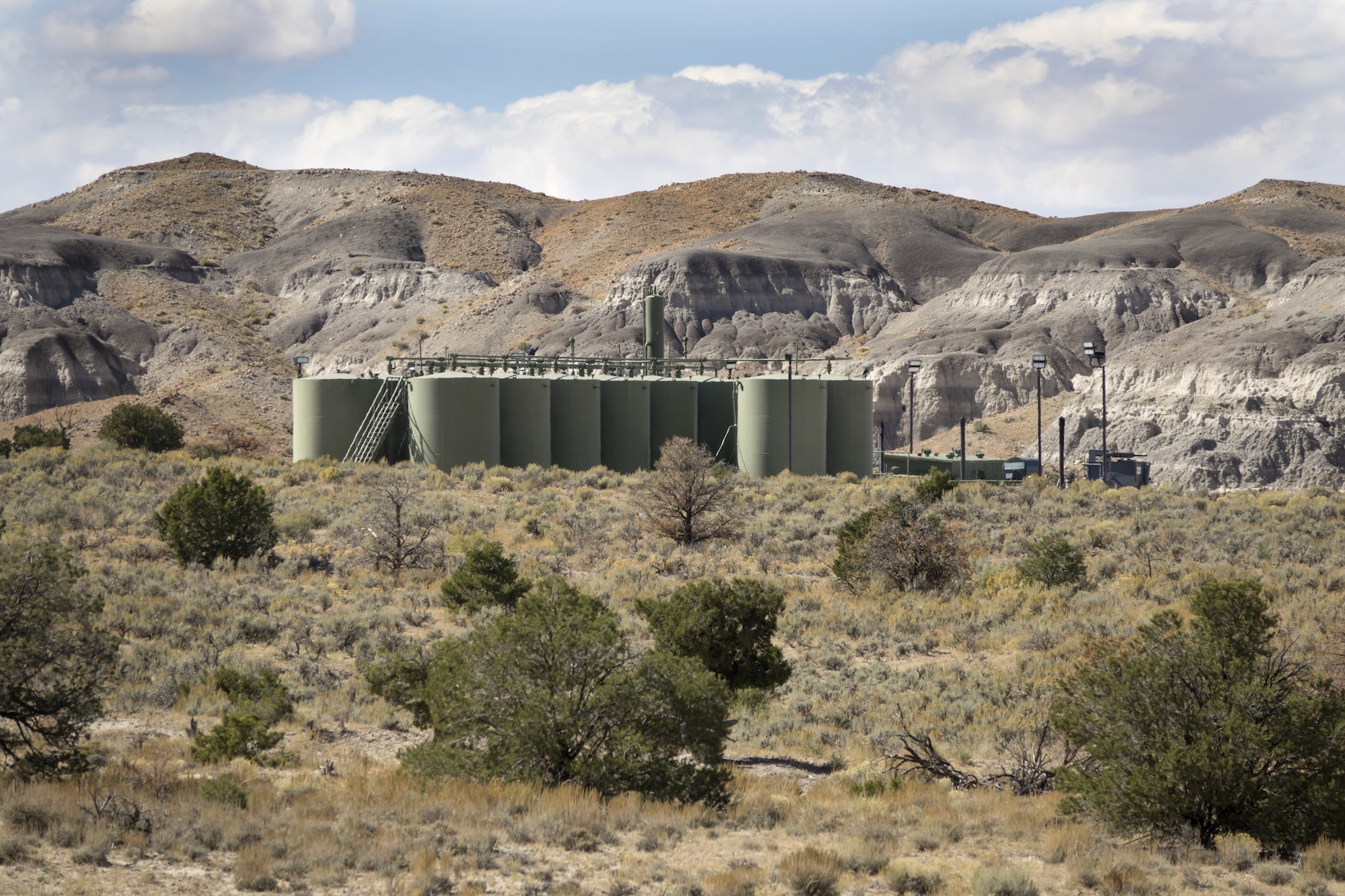 big green-gray storage tanks cluster together in a desert landscape with blue sky