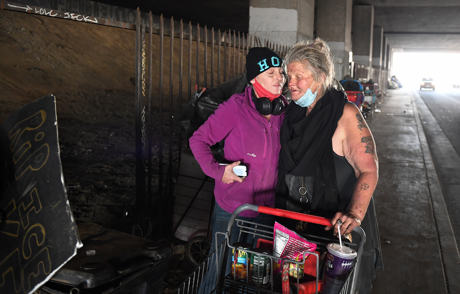 Unhoused women that both go by the name Dawn embrace as they get kicked out of a homeless encampment under the 405 freeway in Inglewood Tuesday morning as work crews clean-up personal belongings and trash in preparation for the Super Bowl.