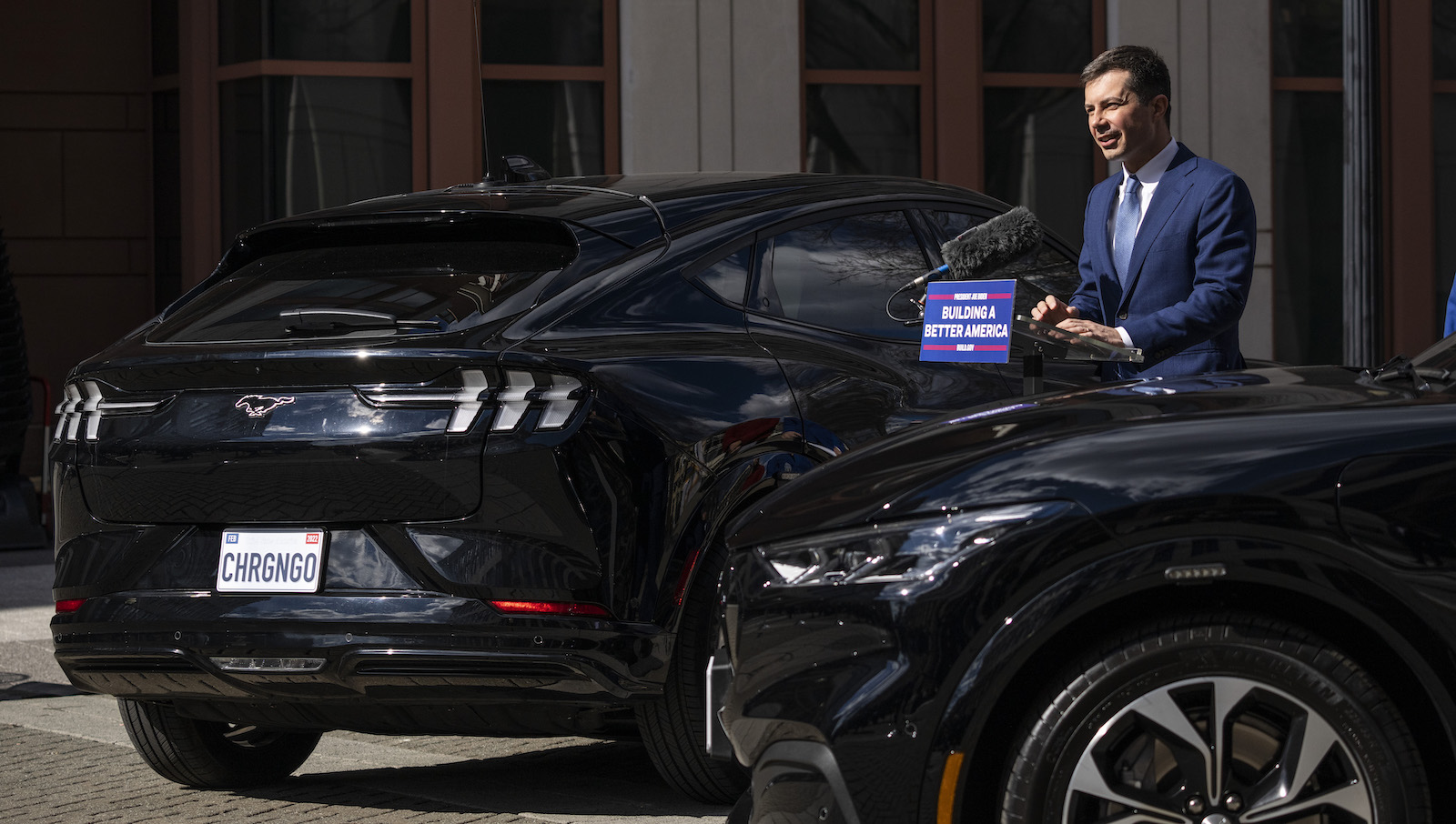 Pete Buttigieg stands between two black electric cars.
