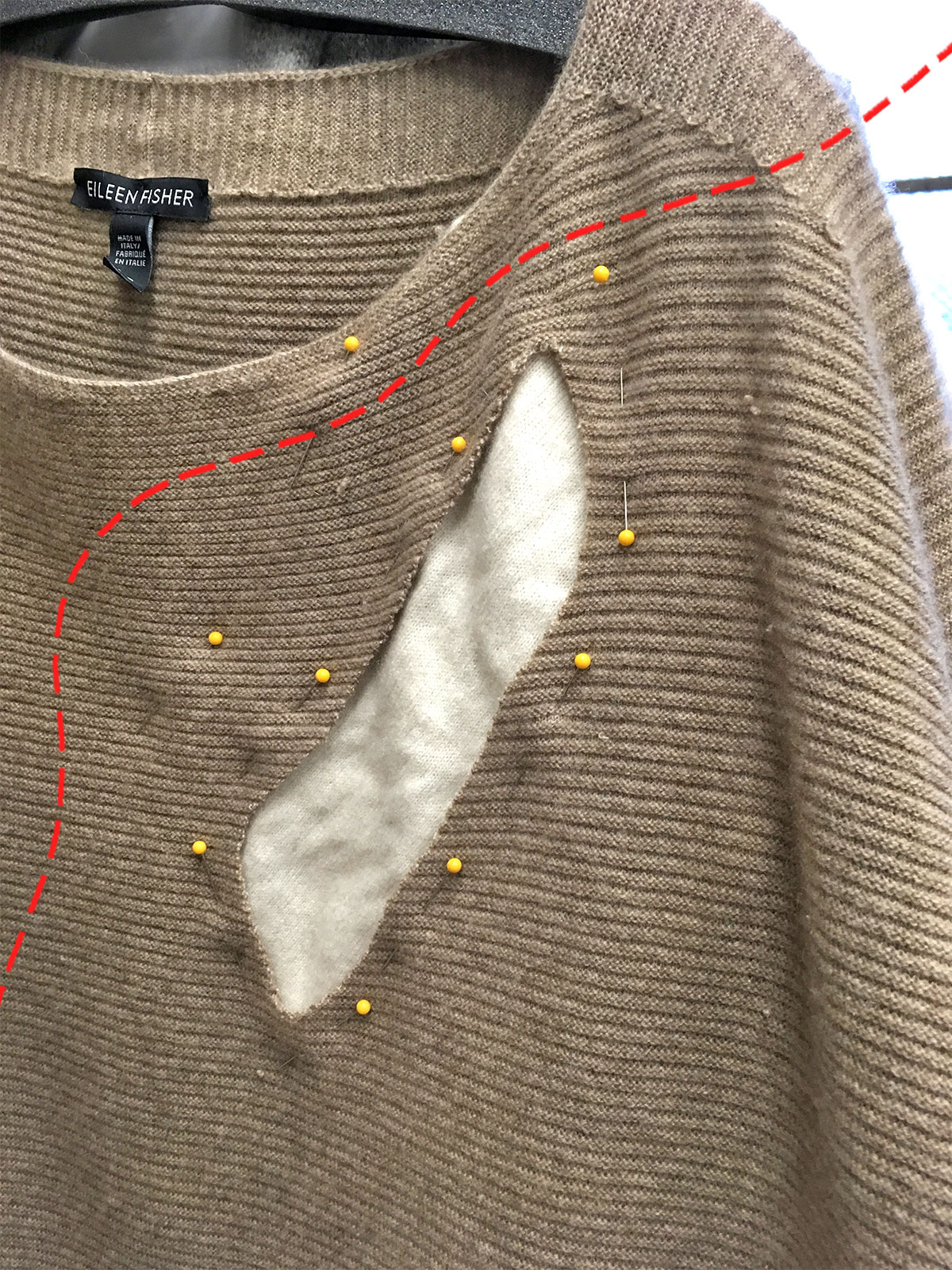 taupe sweater with white patch and yellow pins; drawn red stitches running over photo
