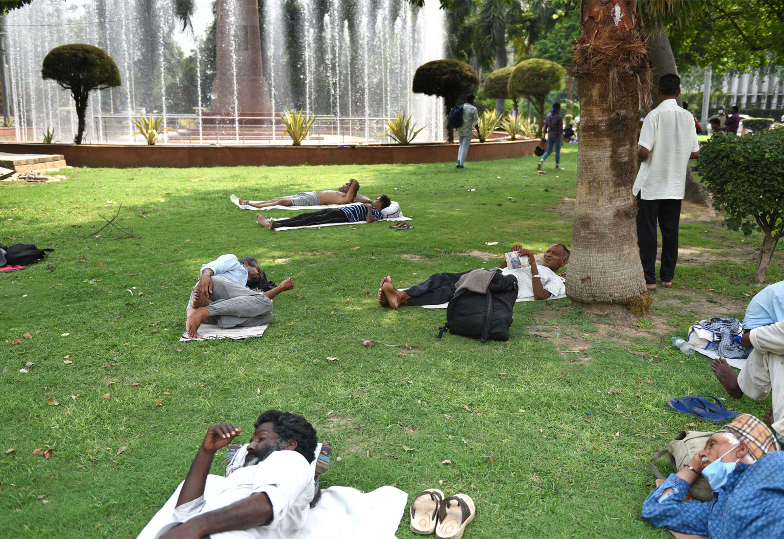 Multiple people in India lying on grass with a fountain in the background