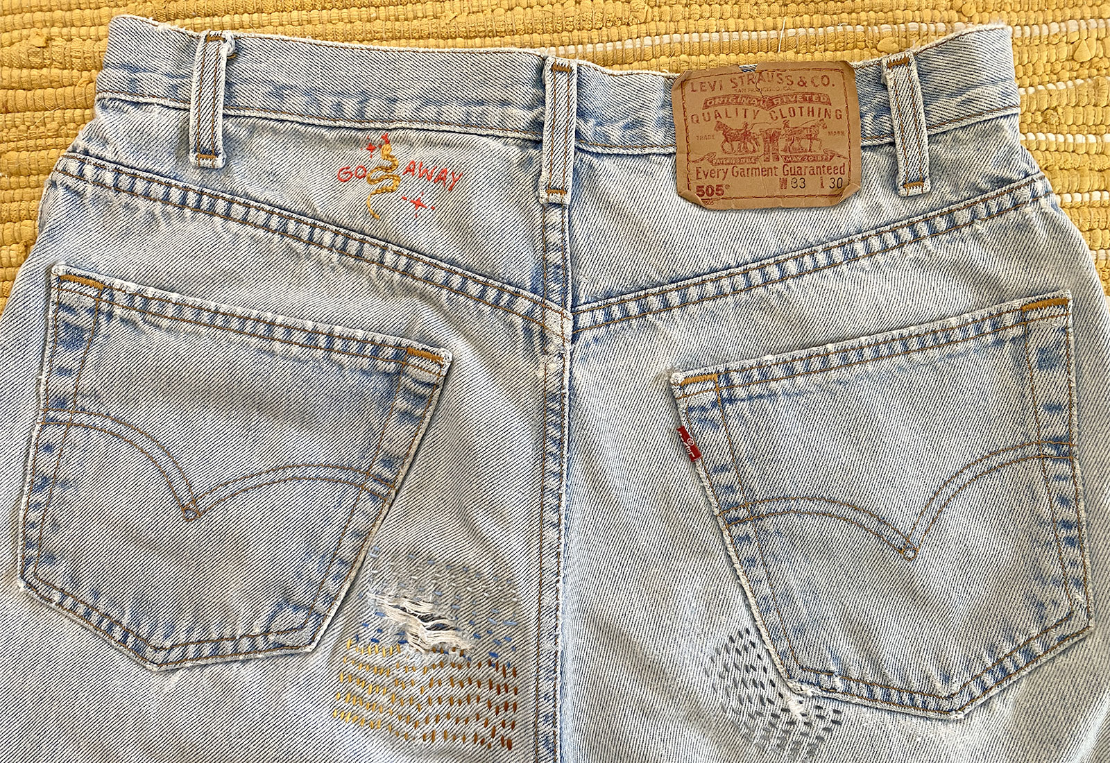 Back view of mended jeans with various running stitches on yellow rug