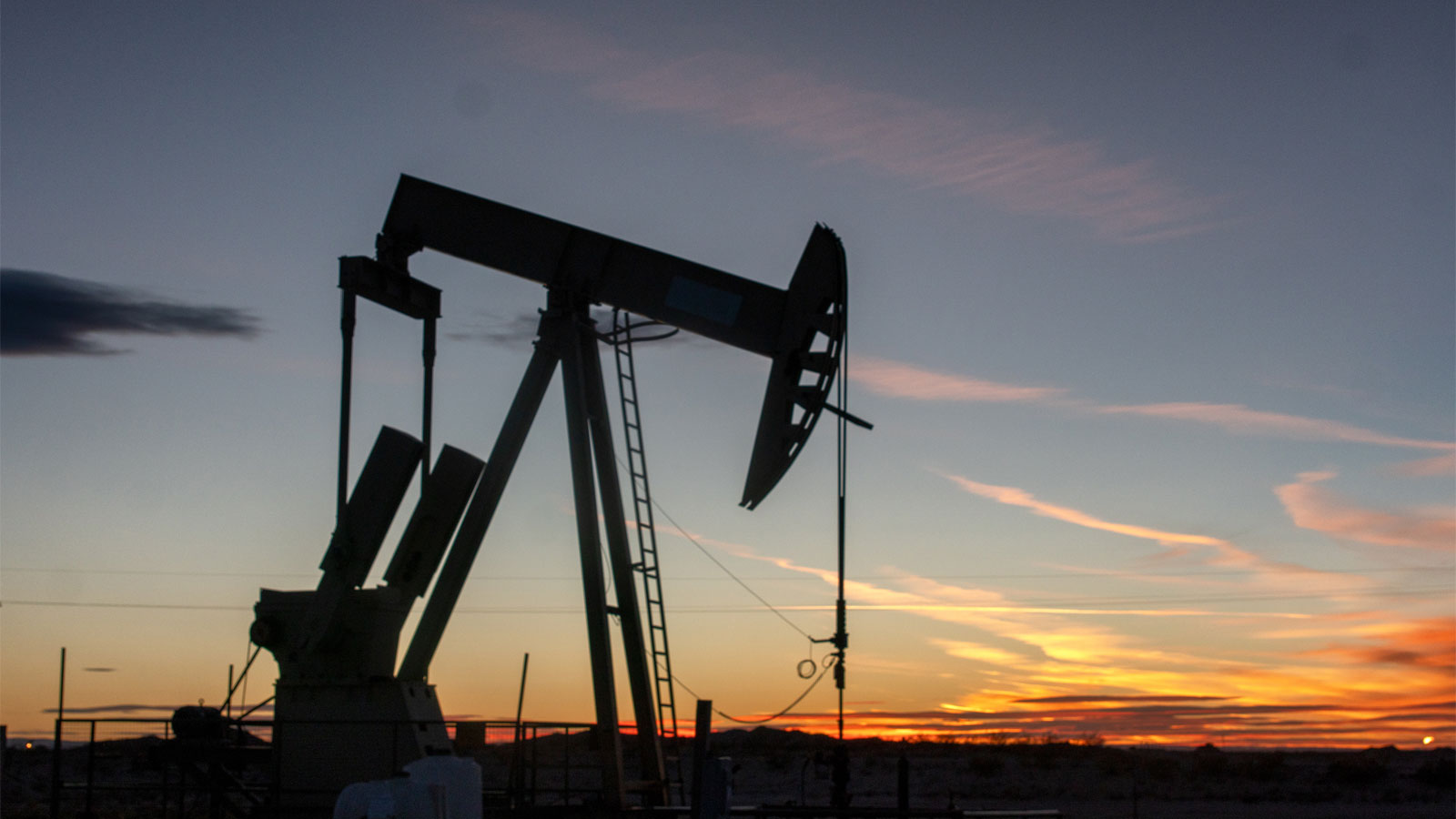 Black silhouette of oil pumpjack with orange sunset in background