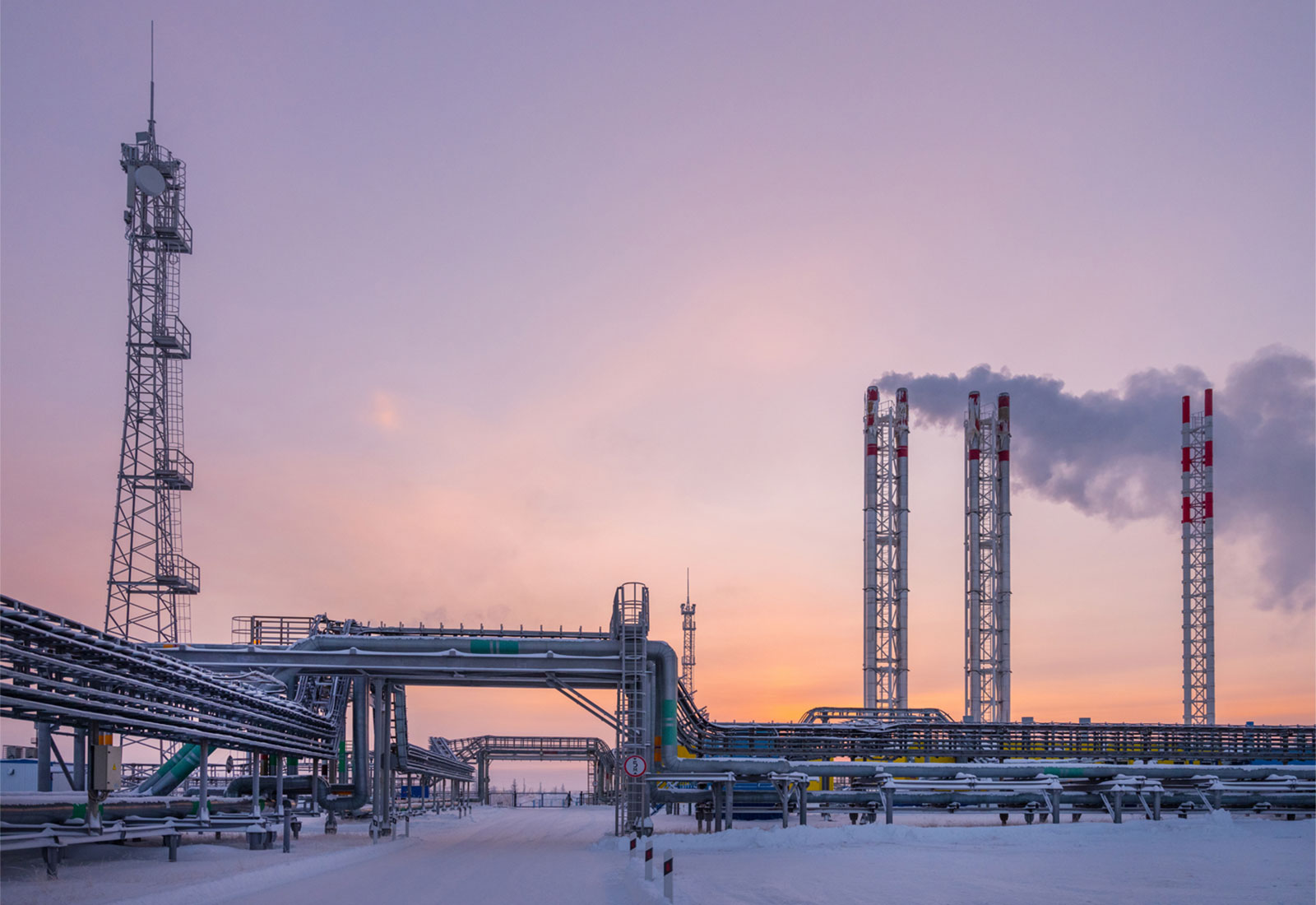 Natural gas refinery pipeline, tower, and smokestacks in front of a sunset