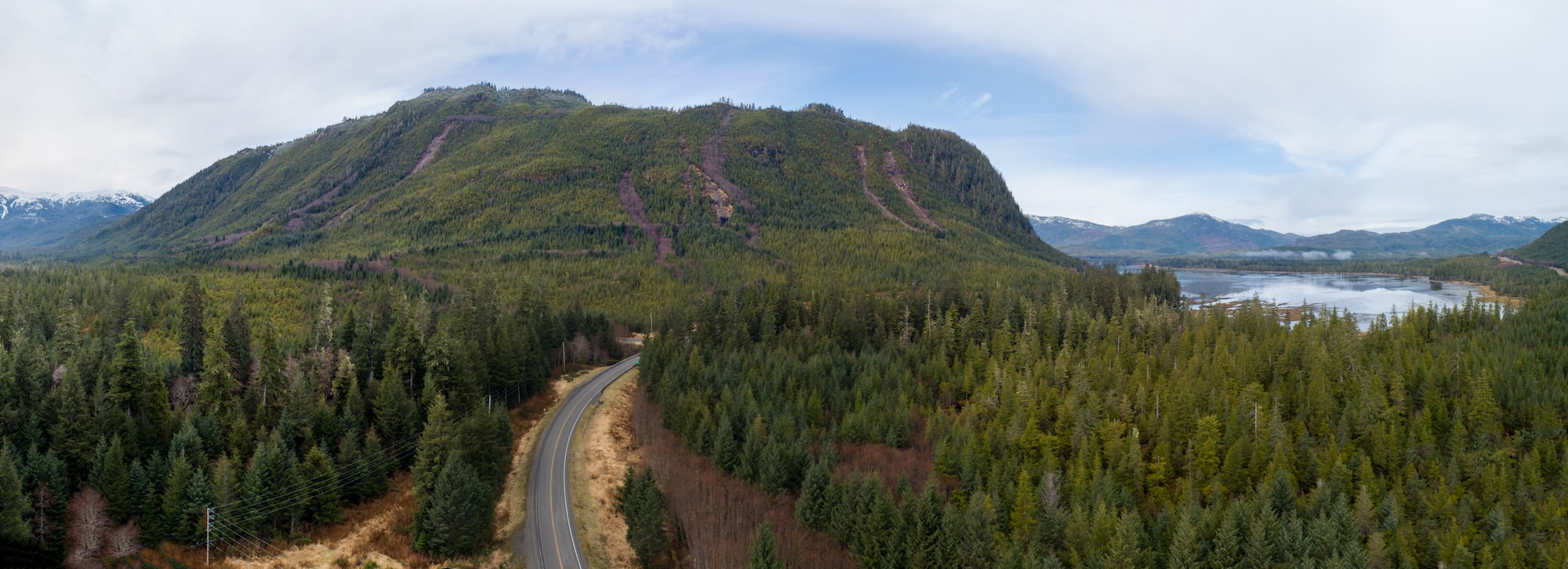 a panoramic view of a road curving into a forested area with large mountain