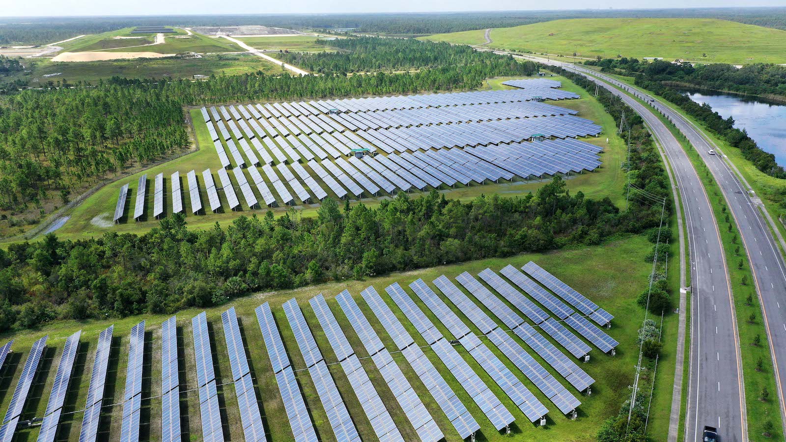 A solar farm spreads out next to a highway and river in this drone footage.
