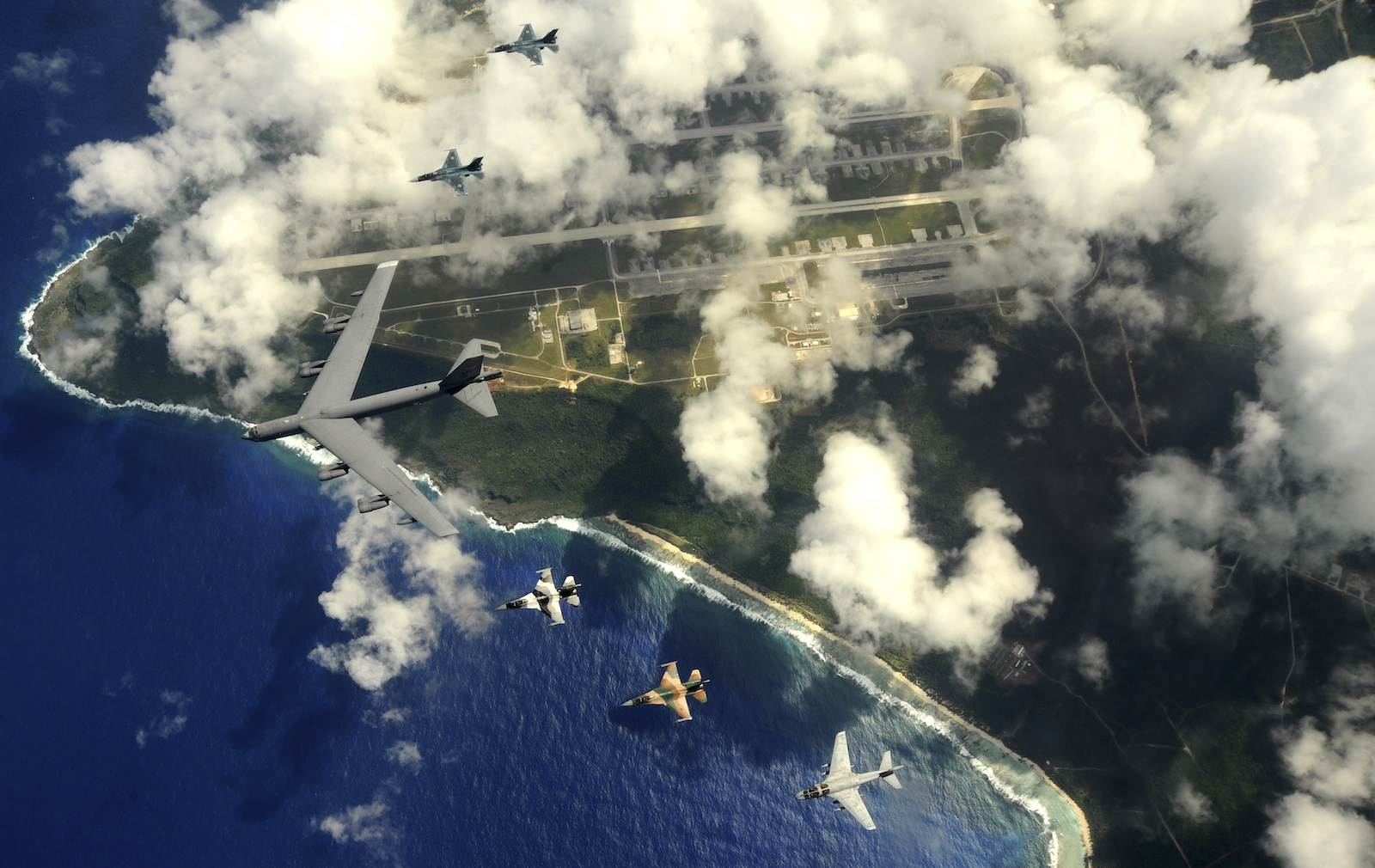 Military planes fly over a point of land and ocean