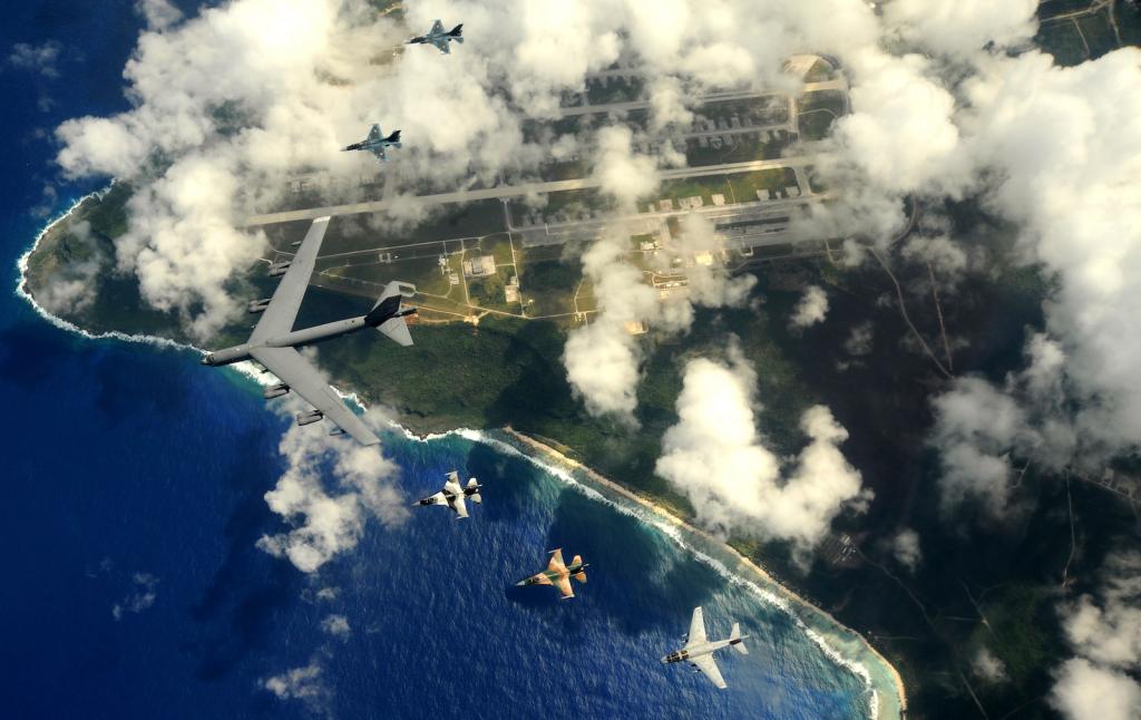 Military planes fly over a point of land and ocean