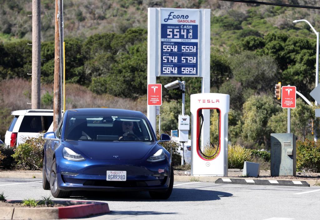 a dark-colored car park at a red and white charging station for electric vehicles in front of a sign stating prices