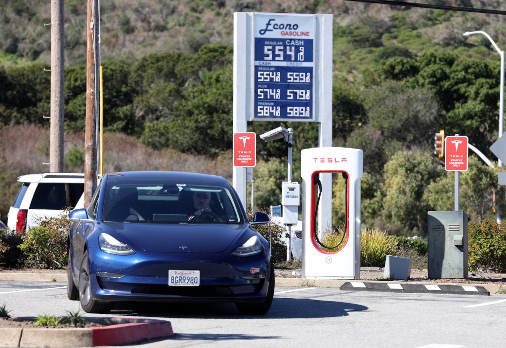 a dark-colored car park at a red and white charging station for electric vehicles in front of a sign stating prices