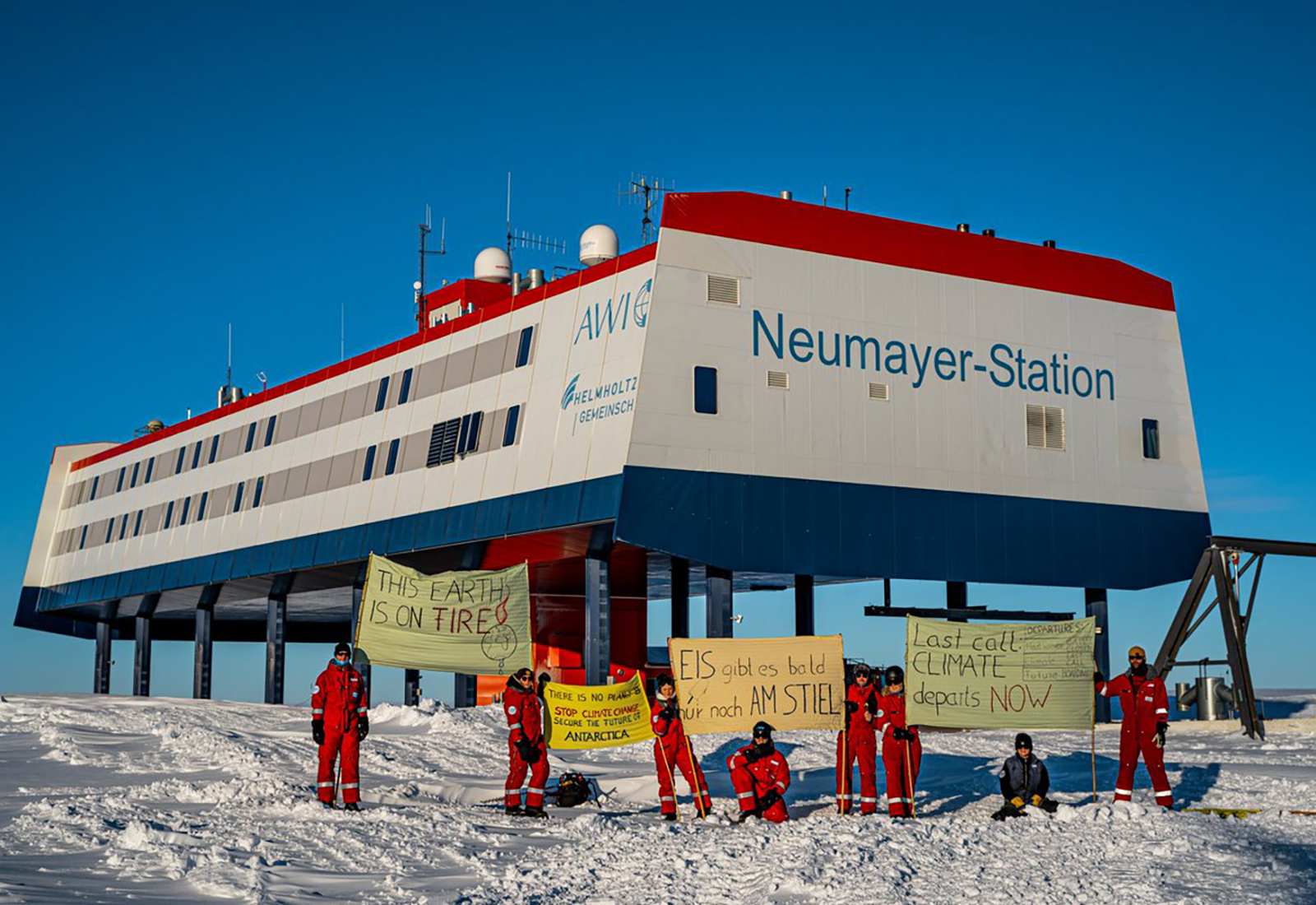 8 people in red snow suits holding signs protesting climate change in front of station in Antarctica